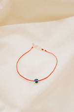 Close-up of silver evil eye charm on red string bracelet