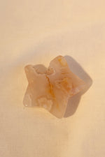 A polished flower agate star-shaped stone with a delicate druzy layer, placed on a textured beige background.