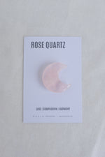 Rose quartz crescent moon stone on a card with text on a light gray background