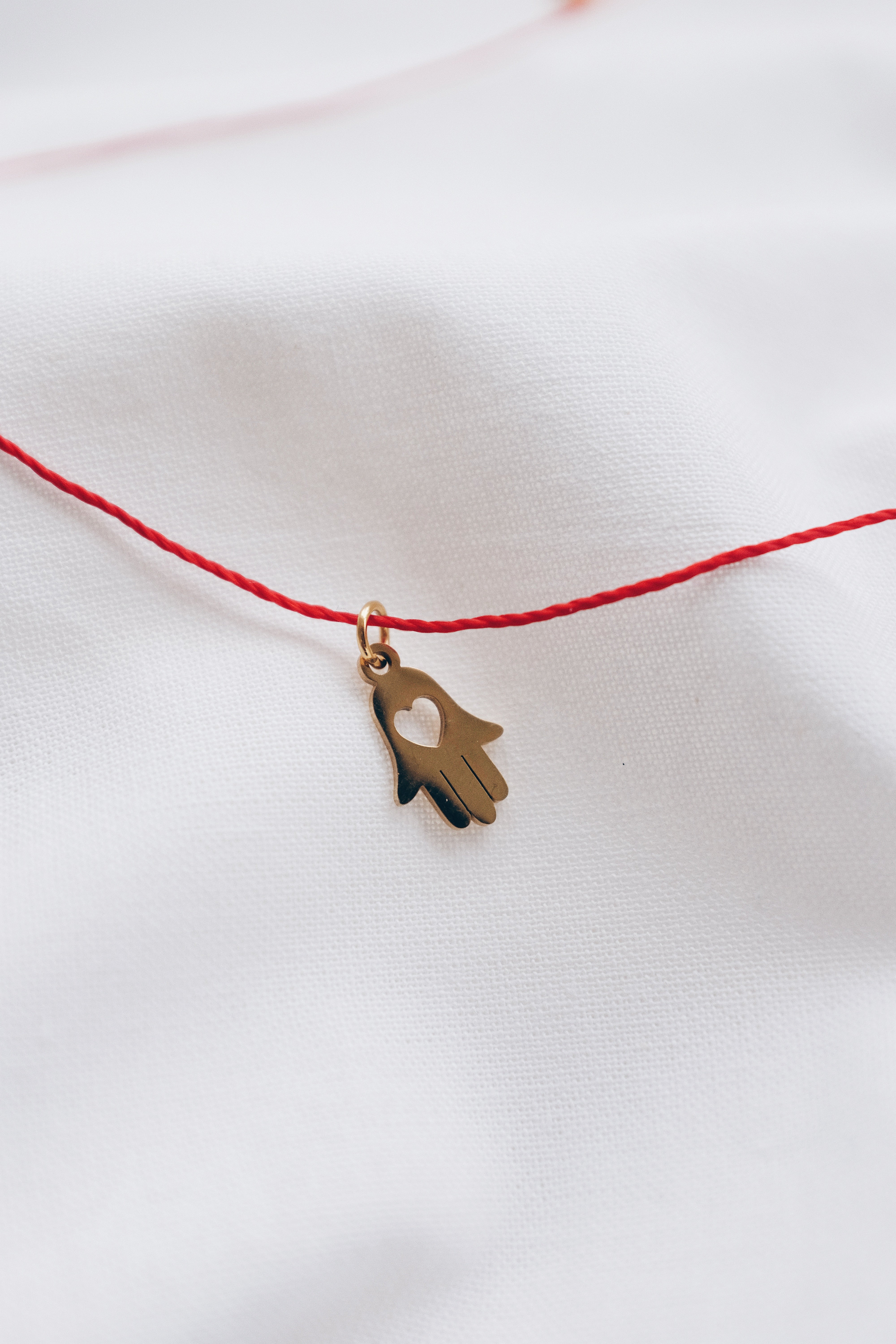 Gold hamsa hand pendant on red string necklace, symbolizing protection and blessings.