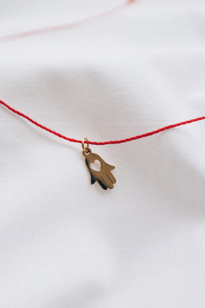 Gold hamsa hand pendant on red string necklace, symbolizing protection and blessings.