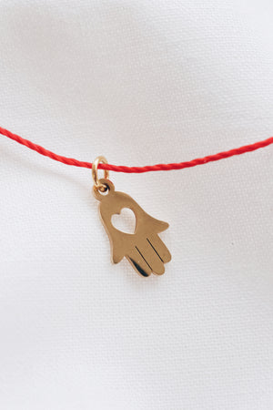 Gold hamsa hand pendant on red string necklace, symbolizing protection and blessings.