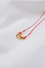 Gold heart pendant with quartz crystal on a red string necklace, symbolizing love and positivity."