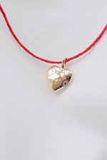 Gold heart pendant with quartz crystal on a red string necklace, symbolizing love and positivity."