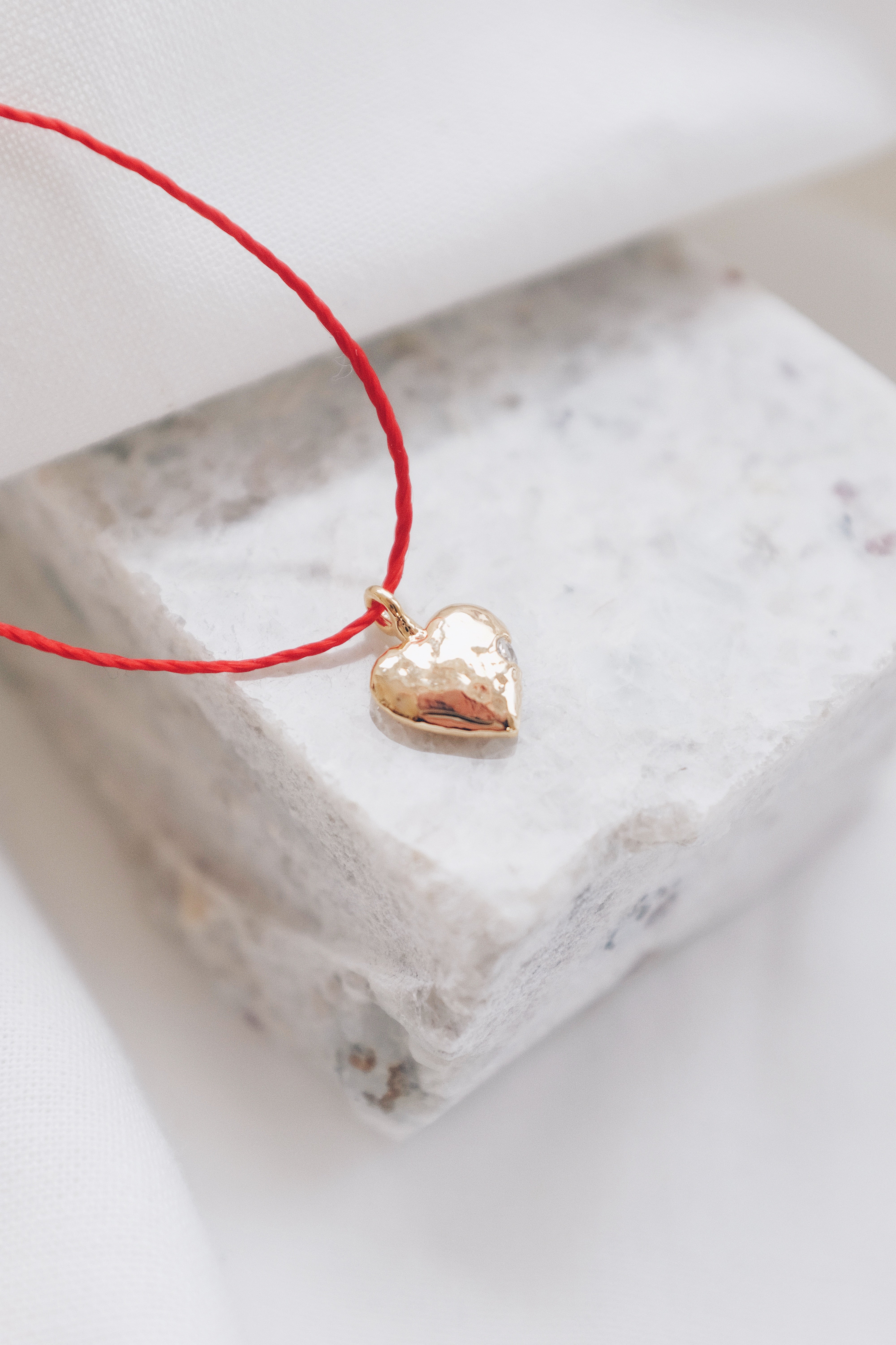 Gold heart pendant with quartz crystal on a red string necklace, symbolizing love and positivity."