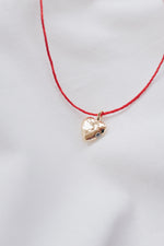 Gold heart pendant with quartz crystal on a red string necklace, symbolizing love and positivity."