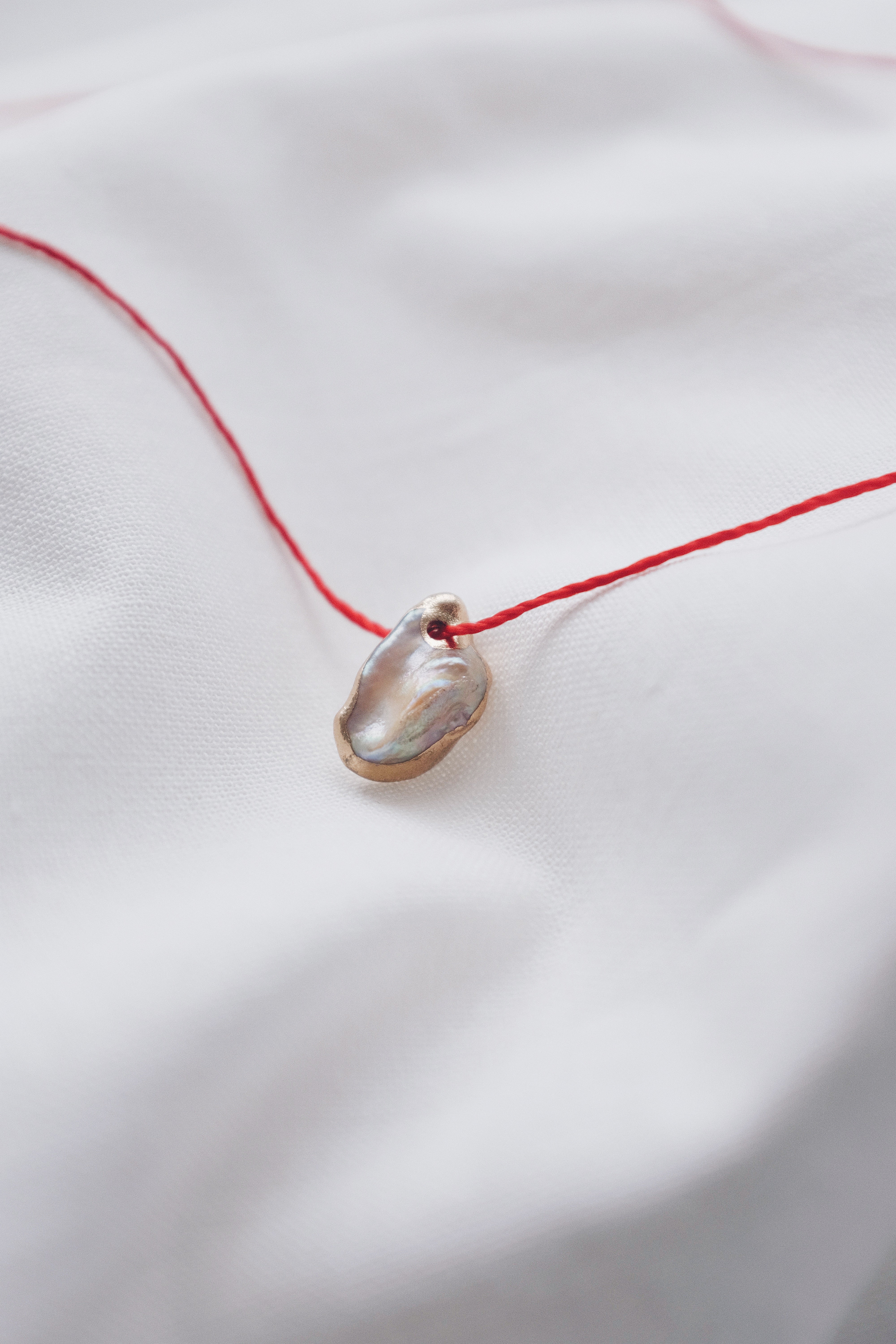 Pearl pendant on a red string necklace, classic and elegant jewelry piece.