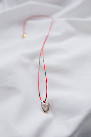 Pearl pendant on a red string necklace, classic and elegant jewelry piece.