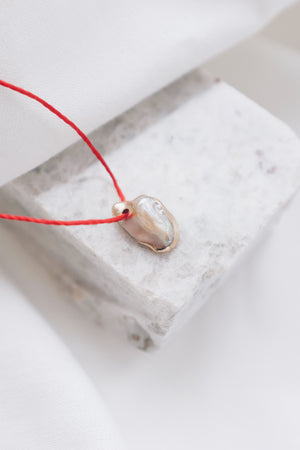 Pearl pendant on a red string necklace, classic and elegant jewelry piece.