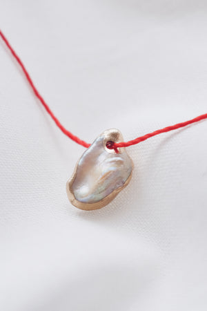 Pearl pendant on a red string necklace, classic and elegant jewelry piece.