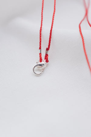 Silver fish pendant on a red string necklace, symbolizing luck and abundance.