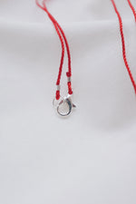 Silver hamsa hand pendant on red string necklace, symbolizing protection and blessings.