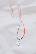 Silver hamsa hand pendant on red string necklace, symbolizing protection and blessings.