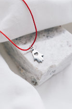 Silver hamsa hand pendant on red string necklace, symbolizing protection and blessings.