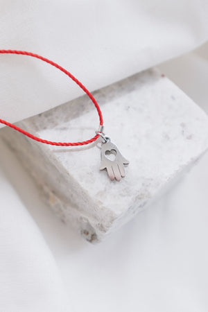 Silver hamsa hand pendant on red string necklace, symbolizing protection and blessings.