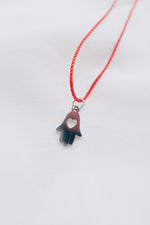 Silver hamsa hand pendant on red string necklace, symbolizing protection and blessings.