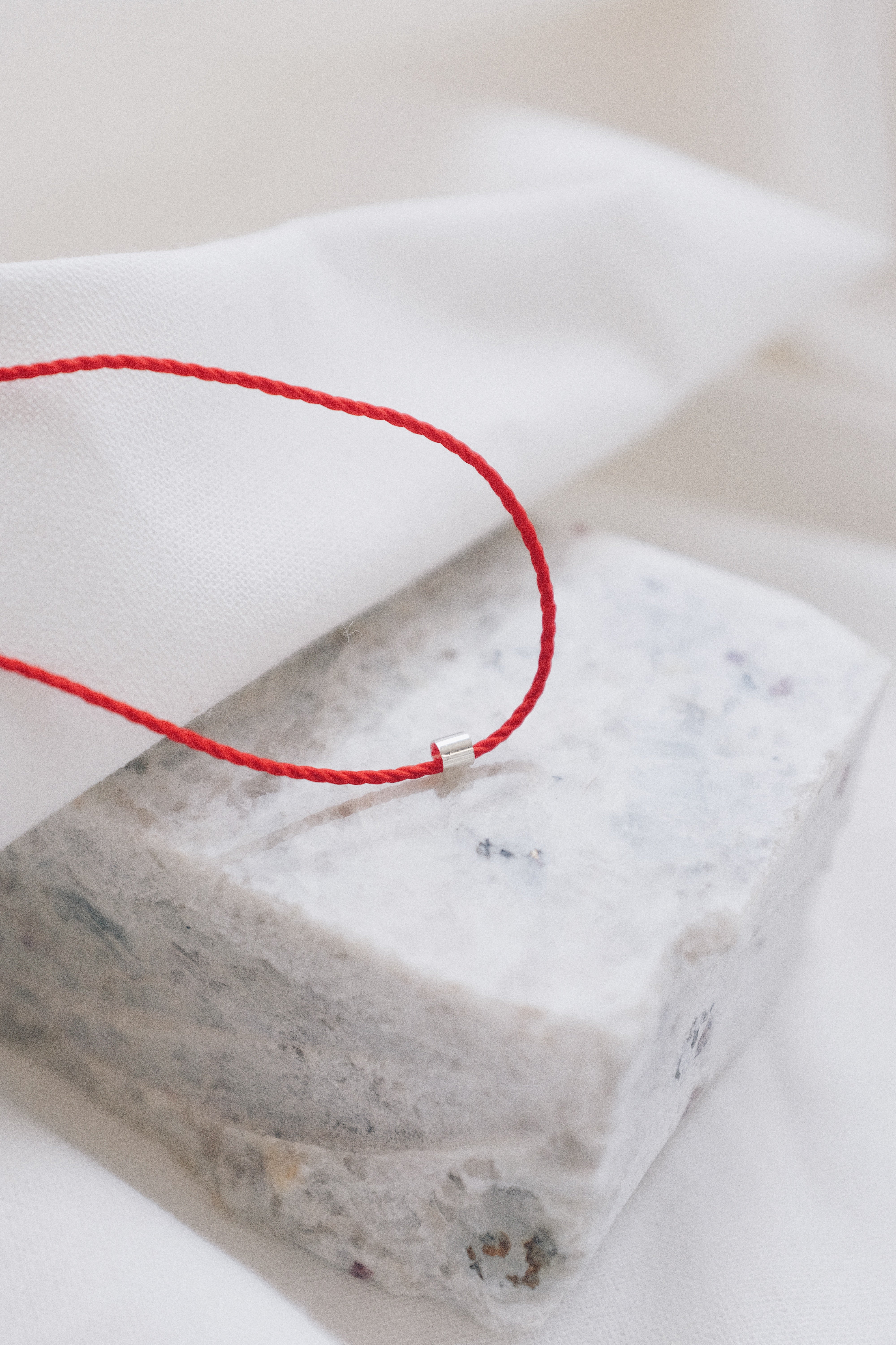 Silver tube pendant on a red string necklace, minimalist and stylish jewelry.